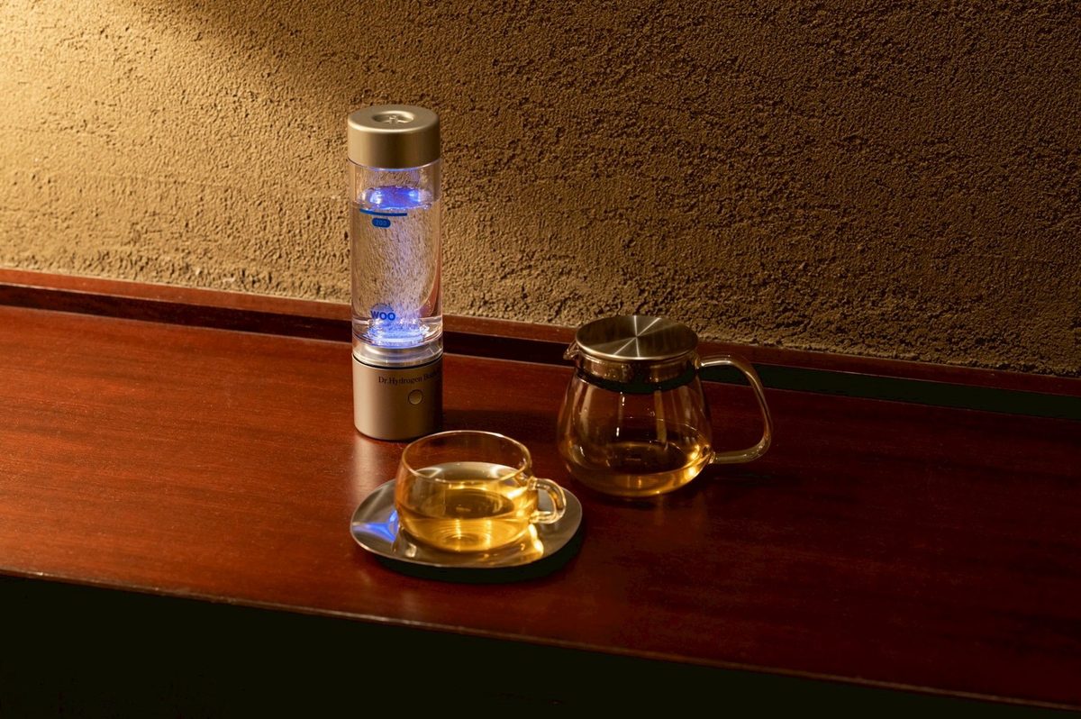 木のカウンターに置いたドクター水素ボトル＋と、お茶の入ったカップ